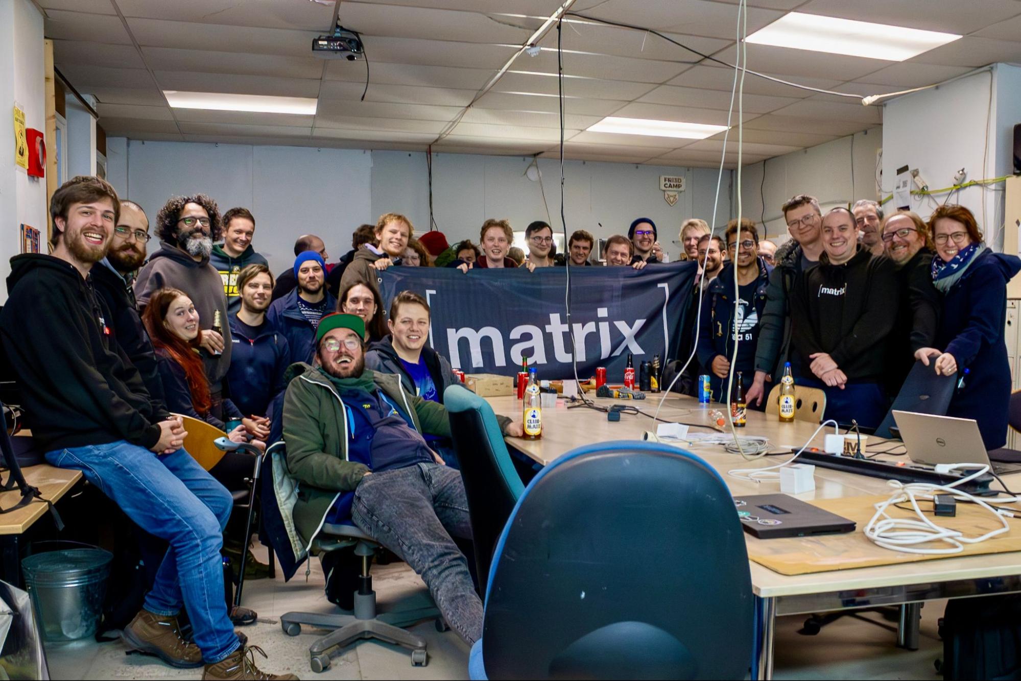 A picture of a group of people smiling, behind a Matrix flag